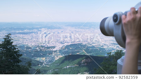 Unrecognizable woman traveler looking through viewing binoculars at summer city. Copy space. Woman observes of blur panorama, with binoculars at observation deck. Mountain Dajti Albania Unrecognizable woman traveler looking through viewing binoculars at summer city. Copy space. Woman observes of blur panorama, with binoculars at observation deck. Mountain Dajti Albania 92582359
