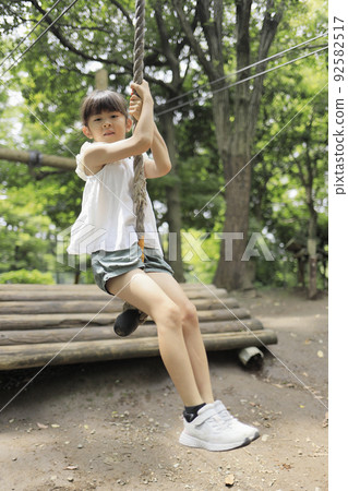 Elementary school girl playing with Tarzan rope (7 years old) Elementary school girl playing with Tarzan rope (7 years old) 92582517