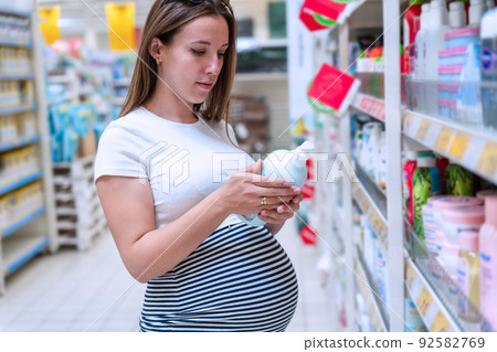 Baby shampoo pregnancy woman buy. Young pregnant woman shopping on baby bath shampoo bottle on supermarket background. Baby cosmetic shop choice. 92582769