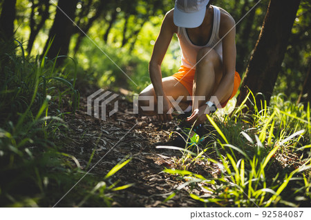 Woman runner tying shoelace on forest trail 92584087