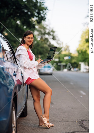 A young woman uses a laptop near a car 92584981