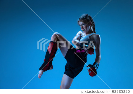 Studio shot of sportive teen-girl, MMA fighter in action, motion isolated on blue background in neon light. Concept of sport, competition, action, achievements Studio shot of sportive teen-girl, MMA fighter in action, motion isolated on blue background in neon light. Concept of sport, competition, action, achievements 92585230