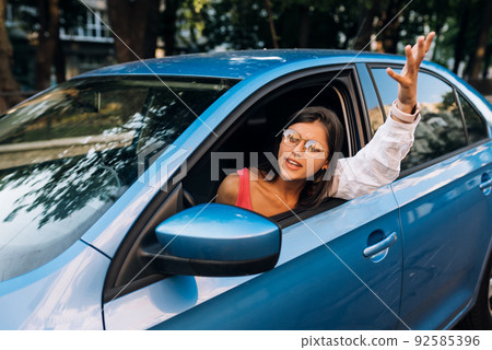 A young angry woman peeks out of the car window A young angry woman peeks out of the car window 92585396