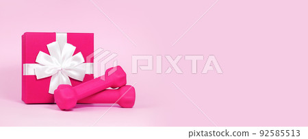 Pink dumbbells near gift box with bow isolated on pink background. Concept of discount, gift or surprise for fitness, home workout, activity and sport, healthy lifestyle. Women Health. Banner 92585513
