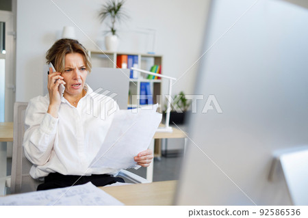 Business woman with a surprised face talking on the phone while looking at documents Business woman with a surprised face talking on the phone while looking at documents 92586536