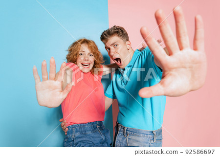 Portrait of young couple with terrified expression, watching horror movie isolated over pink blue studio background 92586697