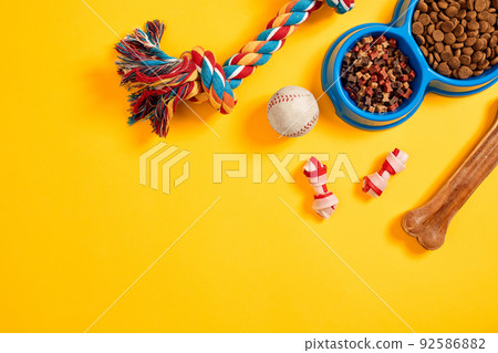 Toys -multi coloured rope, ball and dry food. Accessories for play on yellow background top view Toys -multi coloured rope, ball and dry food. Accessories for play on yellow background top view 92586882