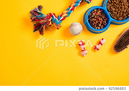 Toys -multi coloured rope, ball and dry food. Accessories for play on yellow background top view Toys -multi coloured rope, ball and dry food. Accessories for play on yellow background top view 92586883