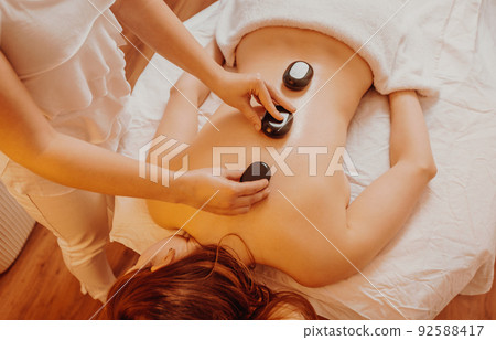 Woman making massages by lava stones in a beauty saloon, lifestyle and healthcare concept Woman making massages by lava stones in a beauty saloon, lifestyle and healthcare concept 92588417