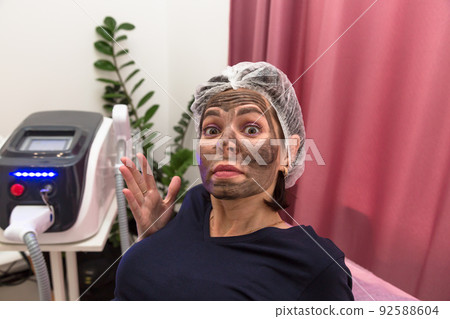 Woman with face smeared with carbon mask in beauty salon Woman with face smeared with carbon mask in beauty salon 92588604