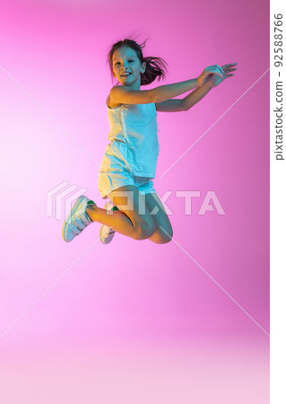 Happy little beautiful girl, school girl in casual outfit isolated on pink background in neon. Concept of children emotions, fashion, beauty, ad 92588766