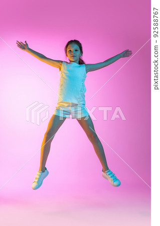 Happy little beautiful girl, school girl in casual outfit isolated on pink background in neon. Concept of children emotions, fashion, beauty, ad 92588767