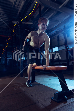 Portrait of young shirtless muscular man training, doing exercises with dumbbells isolated over gym interior Portrait of young shirtless muscular man training, doing exercises with dumbbells isolated over gym interior 92589177