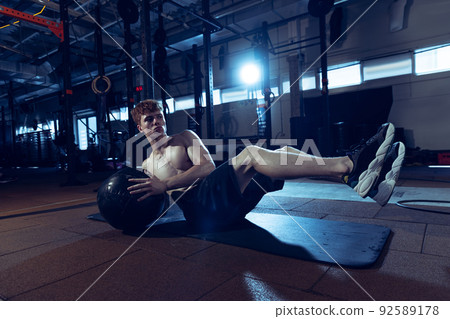 Portrait of young sportive, muscular man doing press exercises with fitness, medicine ball isolated over gym background. Portrait of young sportive, muscular man doing press exercises with fitness, medicine ball isolated over gym background. 92589178