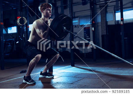 Portrait of young shirtless man training, doing exercises with barbell isolated over gym background. Pulling up Portrait of young shirtless man training, doing exercises with barbell isolated over gym background. Pulling up 92589185