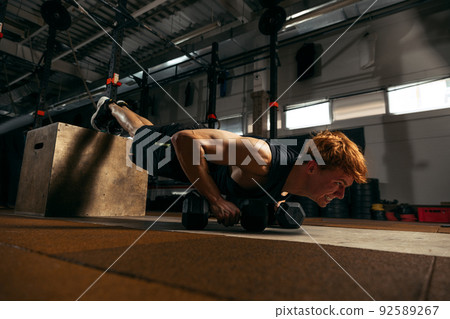 Portrait of young sportive red-headed man doing push up exercises with dumbbells isolated on indoor gym background Portrait of young sportive red-headed man doing push up exercises with dumbbells isolated on indoor gym background 92589267