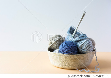 Gray and blue balls of thread in a beige basket with knitting needles for knitting warm clothes, knitting hobby Gray and blue balls of thread in a beige basket with knitting needles for knitting warm clothes, knitting hobby 92589302