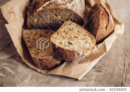Brown fresh bread with seeds are cut into pieces on old wood background. Top view, copy space 92589803