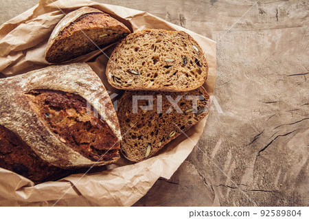 Brown fresh bread with seeds are cut into pieces on old wood background. Top view, copy space Brown fresh bread with seeds are cut into pieces on old wood background. Top view, copy space 92589804