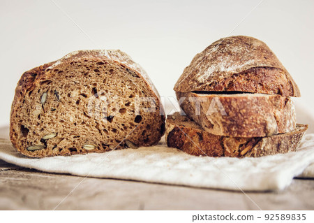 Brown fresh bread with seeds are cut into pieces on old wood background. Copy, empty space for text 92589835