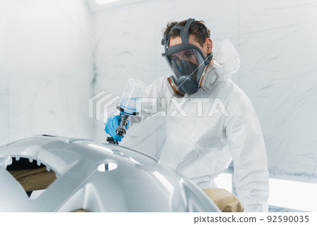 Auto painter varnishing a car body part in a painting booth. Repairman restores vehicle body parts Auto painter varnishing a car body part in a painting booth. Repairman restores vehicle body parts 92590035