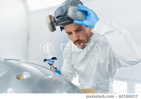Professional car painter in the painting booth takes off his protective mask to check the quality of the work done. Auto painter during work 92590037
