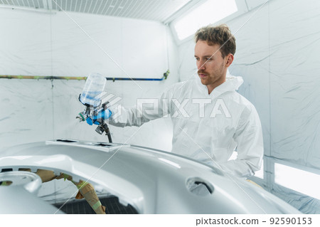 Young curly car painter varnishes a car bumper. Man works in a spray booth. Process of painting car body parts 92590153