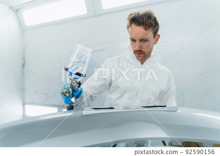 Young curly car painter varnishes a car bumper. Man works in a spray booth. Process of painting car body parts Young curly car painter varnishes a car bumper. Man works in a spray booth. Process of painting car body parts 92590156