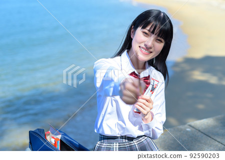 坐在美麗的海邊防波堤上吃巧克力棒狀糖果的高中女生 放學後的海灘約會 92590203