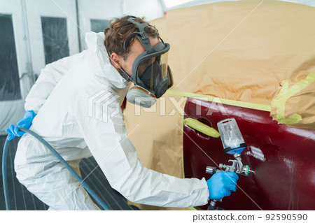 Auto painter in a protective suit and mask sprays a thinner or other cleaner on a car door using a spray gun. Preparation of vehicle body elements for local repair 92590590