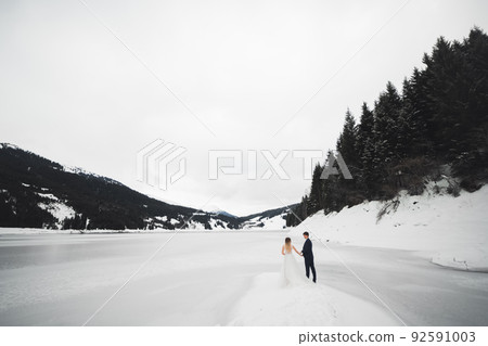 Romantic young couple looking away, back view, lake and winter mountains on background Romantic young couple looking away, back view, lake and winter mountains on background 92591003