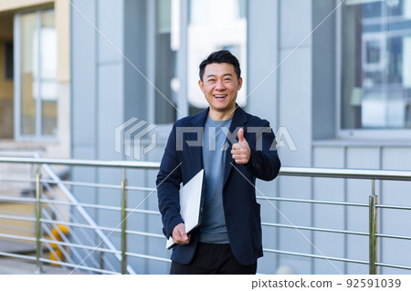 portrait handsome Asian man a university college teacher, businessman, scientist or educator. Standing background modern office center or campus with arms crossed Outside, outdoors looking at camera portrait handsome Asian man a university college teacher, businessman, scientist or educator. Standing background modern office center or campus with arms crossed Outside, outdoors looking at camera 92591039