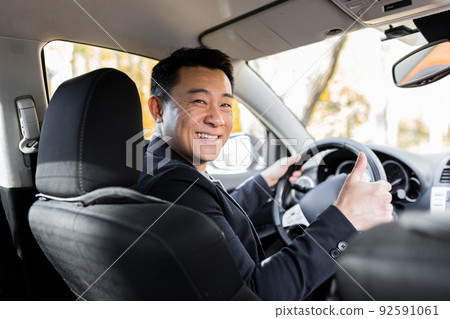A man driving an Asian car behind the wheel looks at the camera and smiles A man driving an Asian car behind the wheel looks at the camera and smiles 92591061