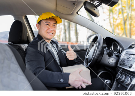 Male courier asian looks into the camera and smiles holding a parcel sitting in the car Male courier asian looks into the camera and smiles holding a parcel sitting in the car 92591063
