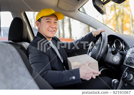 Male courier asian looks into the camera and smiles holding a parcel sitting in the car Male courier asian looks into the camera and smiles holding a parcel sitting in the car 92591067