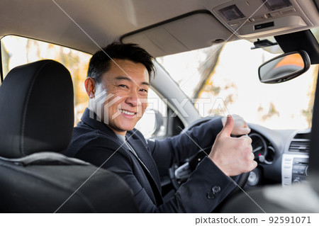 Successful businessman car salesman Male Asian driver behind the wheel looking into the camera and smiling Successful businessman car salesman Male Asian driver behind the wheel looking into the camera and smiling 92591071