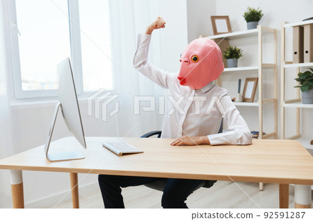 Crazy funny happy businesswoman worker freelancer in pink fish mask work on computer online showing muscles in light modern office. Copy space Crazy funny happy businesswoman worker freelancer in pink fish mask work on computer online showing muscles in light modern office. Copy space 92591287