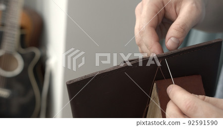 Sewing a brown leather wallet. Leather work. Sewing products by hand. Manufacture of leather goods. Sewing a brown leather wallet. Leather work. Sewing products by hand. Manufacture of leather goods. 92591590
