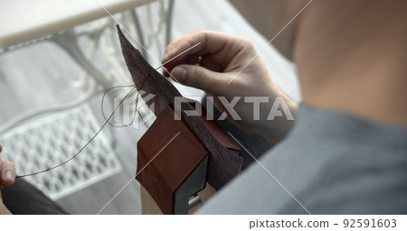 Craftsman sewing a handmade brown leather wallet in workshop. 92591603
