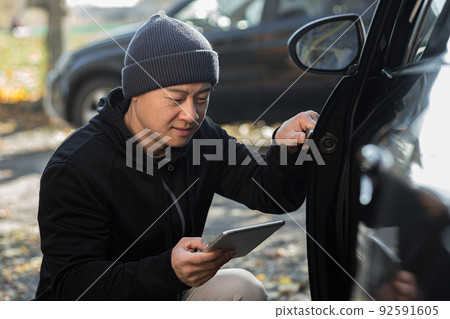 male bandit thief car thief asian uses a tablet to turn off the car alarm male bandit thief car thief asian uses a tablet to turn off the car alarm 92591605