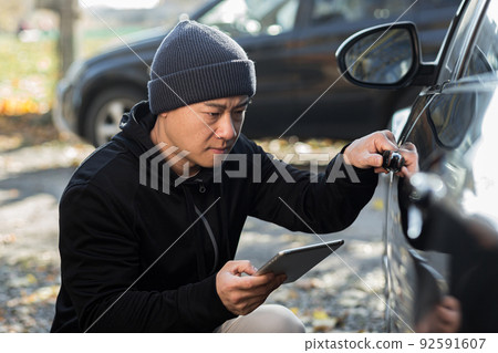 male bandit thief car thief asian uses a tablet to turn off the car alarm 92591607