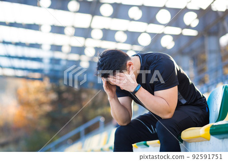 Frustrated Asian male athlete depressed, dissatisfied with the result of his training, in despair after running, resting sitting Frustrated Asian male athlete depressed, dissatisfied with the result of his training, in despair after running, resting sitting 92591751