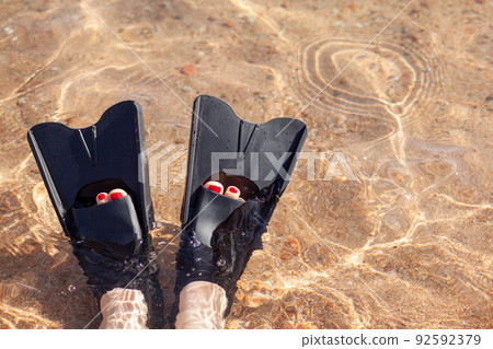 A woman in black flippers splashes near the shore. Fins stick out 92592379