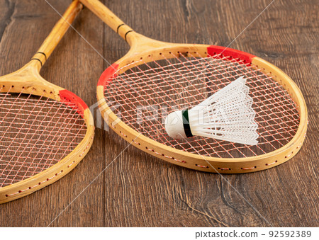 White badminton shuttlecock and two wooden badminton rackets on a wooden background. 92592389