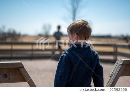 Child waiting along fence for next round of gaga ball in a school playground. Child waiting along fence for next round of gaga ball in a school playground. 92592966