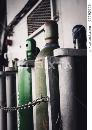 Compressed gas cylinders being stored vertically secured by a metal chain. 92592996