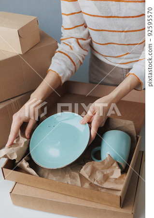 woman entrepreneur sells dishes, plates and cups made of clay, ceramics online and packs them in boxes for sending to the delivery service woman entrepreneur sells dishes, plates and cups made of clay, ceramics online and packs them in boxes for sending to the delivery service 92595570