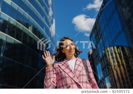business woman in a pink jacket goes to work in the office and smiles. A successful confident European woman entrepreneur  92595572