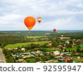Large beautiful hot balloons fly high in the sky over scenery green field and forest. Extreme entertainment for vacation and leisure 92595947