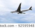 View from below on white passenger plane with the landing gear released flies against the background of the blue sky to land at the airport. 92595948